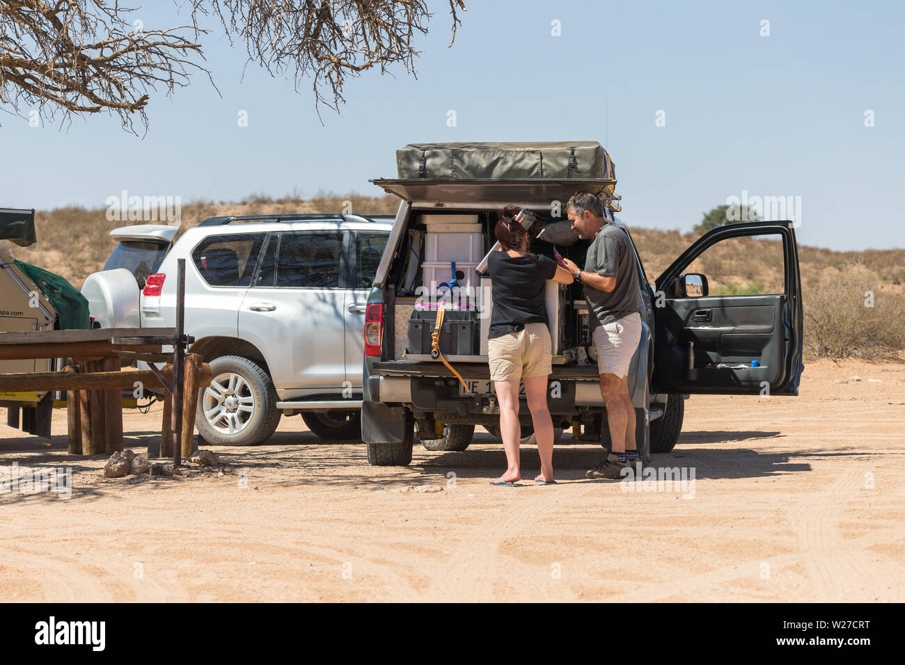Couple ou homme et femme de déballer leurs 4x4 off road camping overland véhicule lors d'un camp site de pique-nique dans le parc transfrontalier de Kgalagadi, Afrique du Sud Banque D'Images