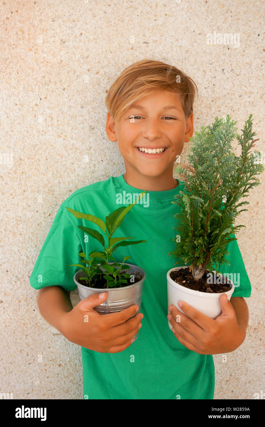 L'enfant blond souriant et portant des T-shirt vert tenant deux pots avec les jeunes plantes Banque D'Images