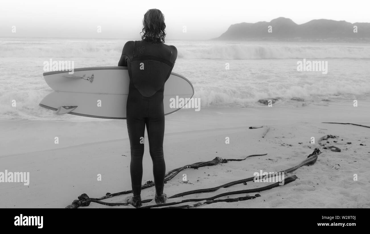 Un surfeur de St James sur Danger Beach envisage de retourner dans la mer tout en regardant une autre série de vagues sur la péninsule du Cap, Afrique du Sud Banque D'Images