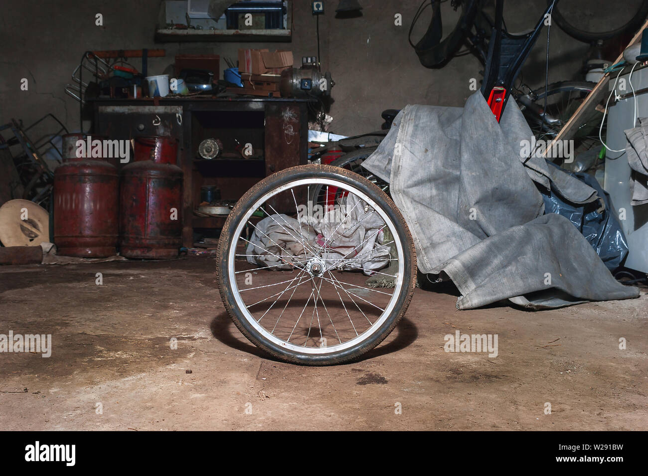 Roue de vélo sale sur le sol d'une maison malpropre avec de l'équipement de garage, Workbench, outils et le tissu en arrière-plan. Banque D'Images
