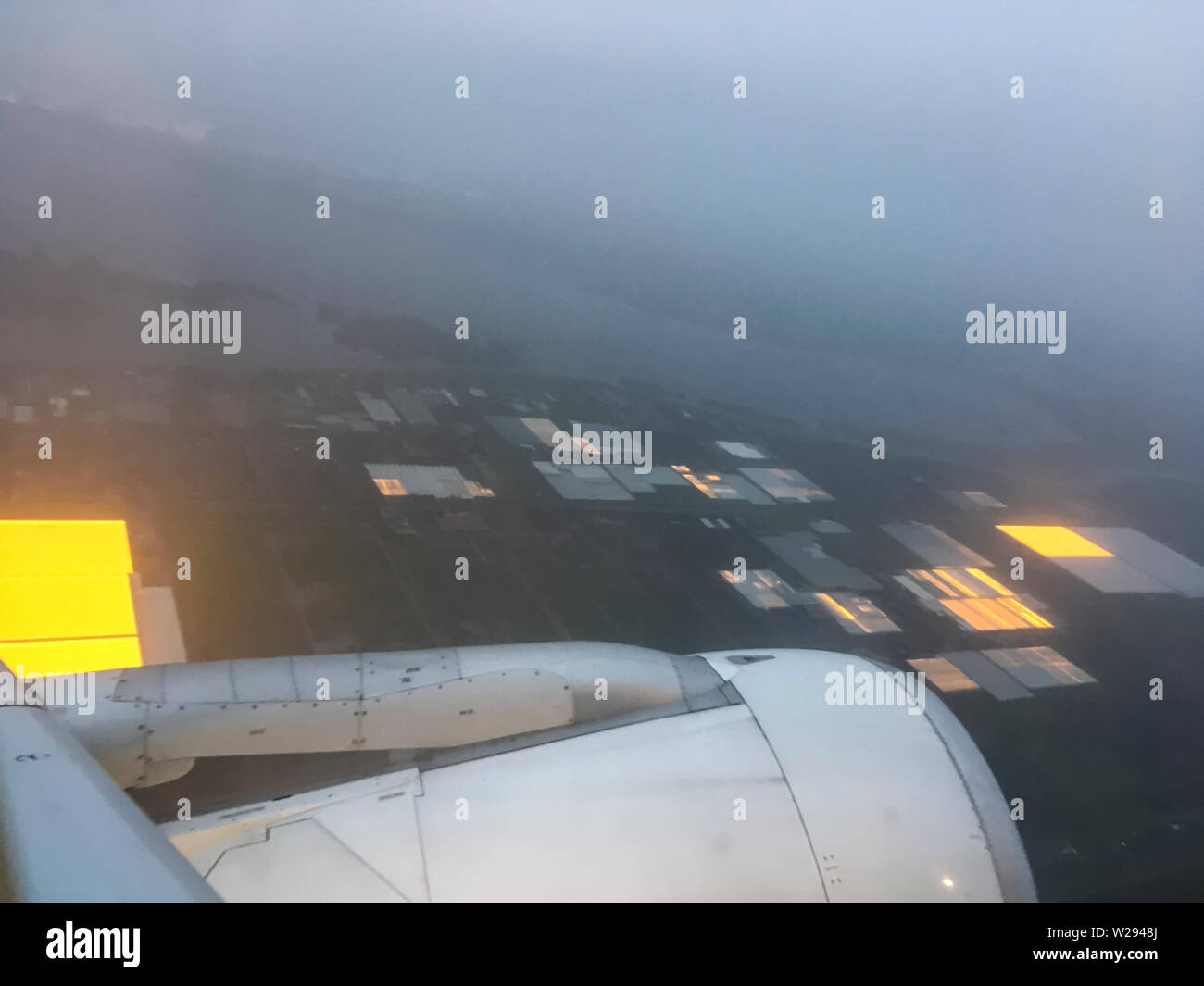Schiphol, Pays-Bas - 21 décembre 2018 : Photographie aérienne d'un grand domaine agricole serres aux Pays-Bas qui sont éclairés à l'intérieur pour une meilleure croissance des produits de la ferme en hiver. Photo prise depuis un avion à l'atterrissage près de l'aéroport Schiphol d'Amsterdam au début de matinée. Banque D'Images