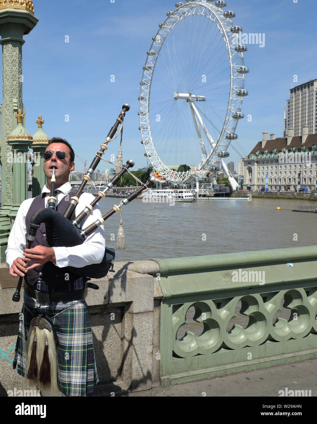 Joueur de cornemuse musicien ambulant en costume traditionnel écossais joue sur le pont de Westminster, Londres UK recevoir... les touristes. Banque D'Images