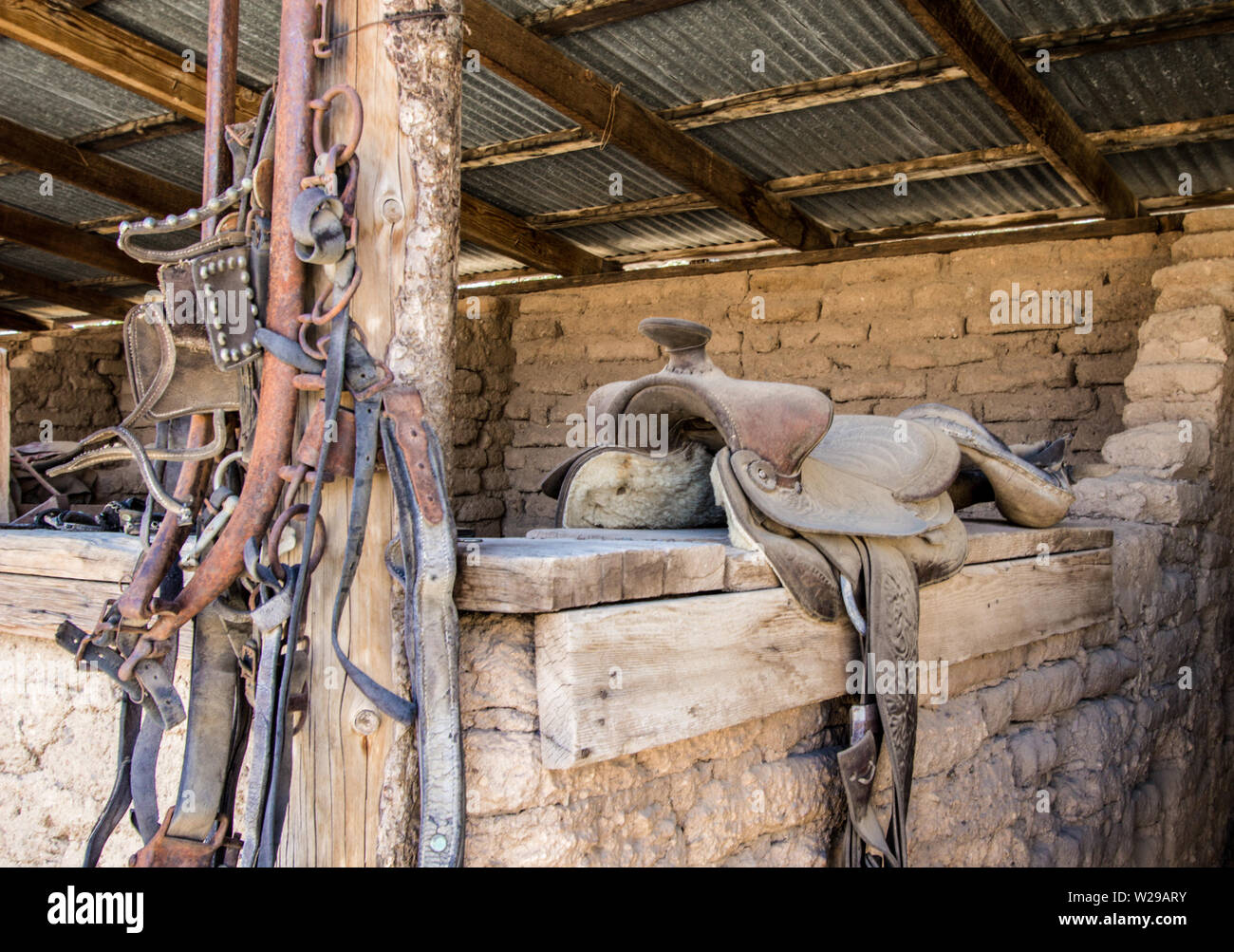 Style occidental Bridle et Saddle. Intérieur de la grange avec une selle d'équitation en cuir usée et craquelée et un groupe de brides de cheval. Banque D'Images