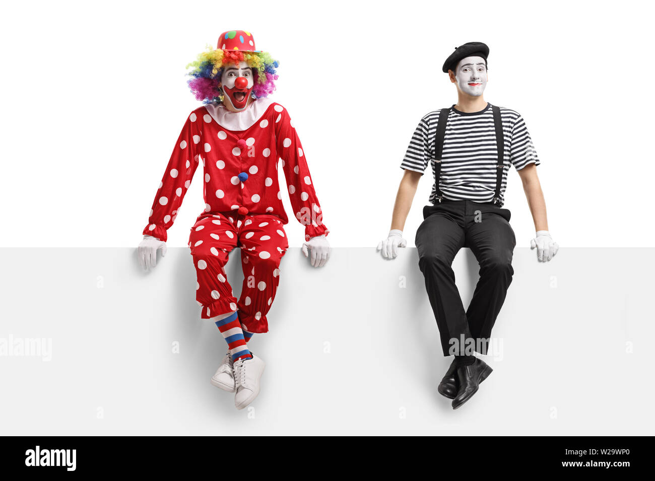 Longueur totale d'un clown et d'un mime assis sur un panneau isolé sur fond blanc Banque D'Images