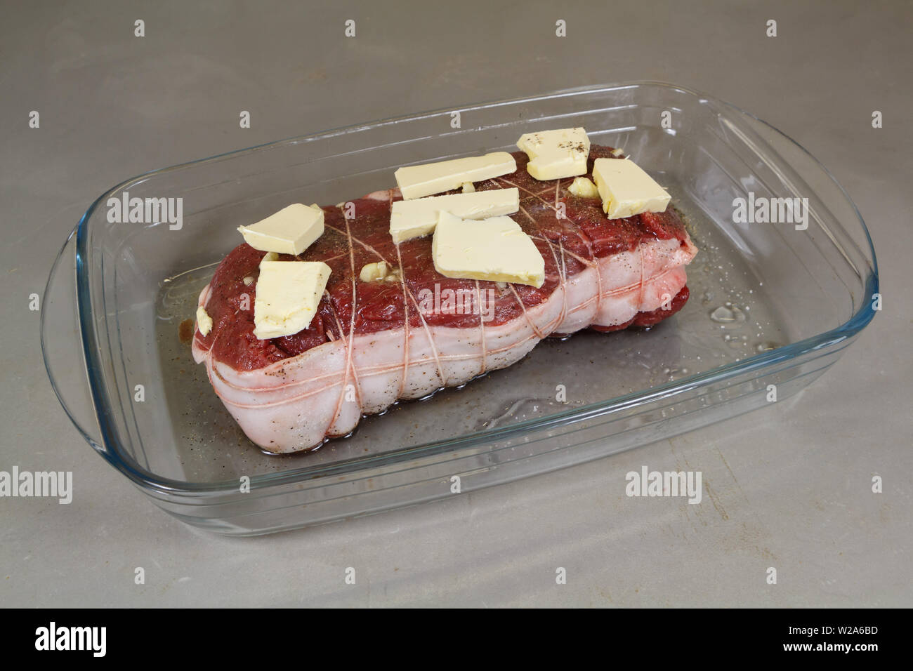 Rôti de bœuf cru avec de la margarine sur un plat en verre avant la cuisson Banque D'Images
