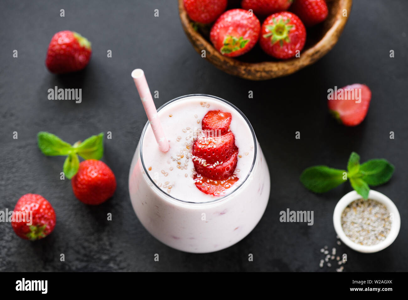 Smoothie aux fraises milkshake ou en verre avec des graines de chia et rose paille sur fond noir Banque D'Images