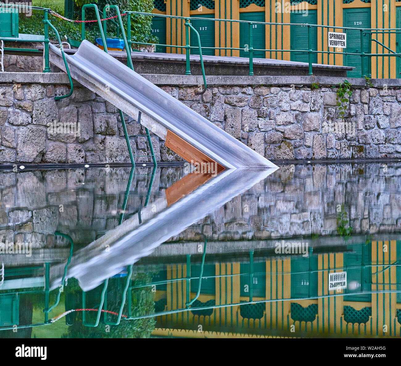 Une piscine thermale naturelle historique à Bad Fischau, Autriche. Un métal glisser dans la piscine et de cabanes en bois avec leur reflet dans l'eau cristalline wate Banque D'Images