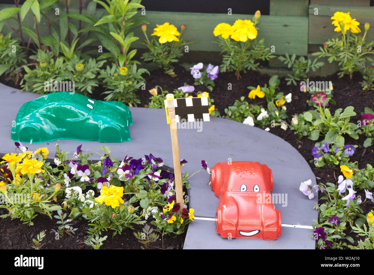 Voitures jouets en plastique sur une piste de course dans le jardin de fleurs Banque D'Images