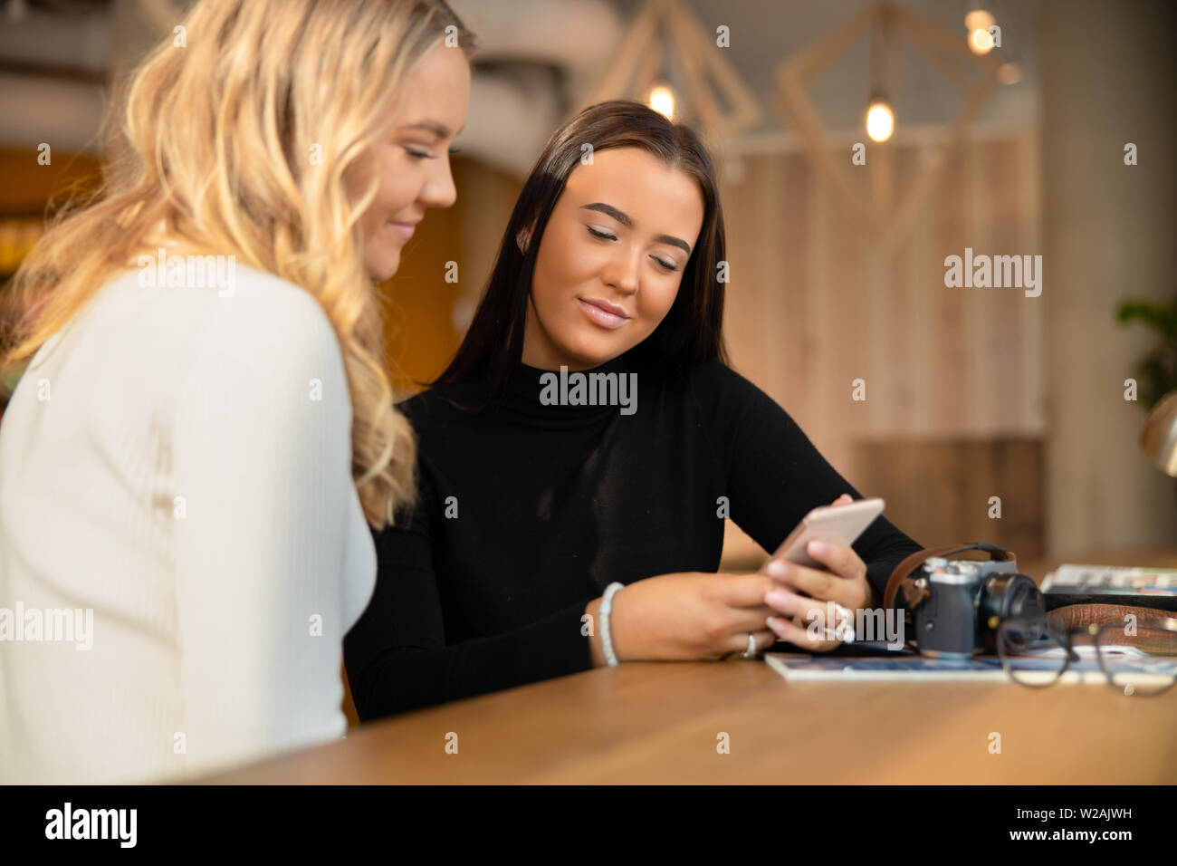 Sourire et deux belles jeunes amis Looking At Smartphone In Cafe Banque D'Images