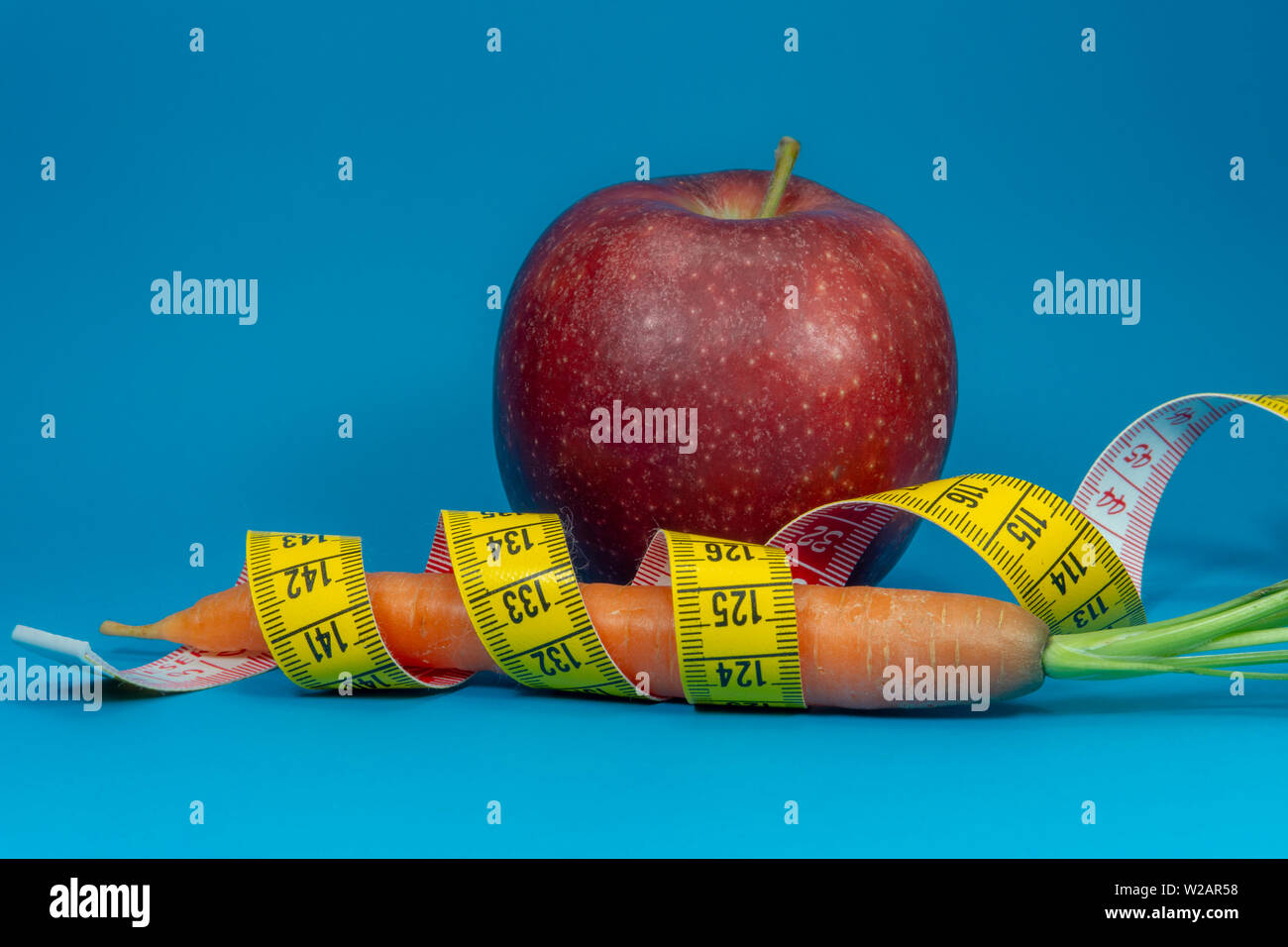 La perte de poids et régime alimentaire sain concept avec un ruban à mesurer, de carotte et de pomme rouge sur fond bleu Banque D'Images