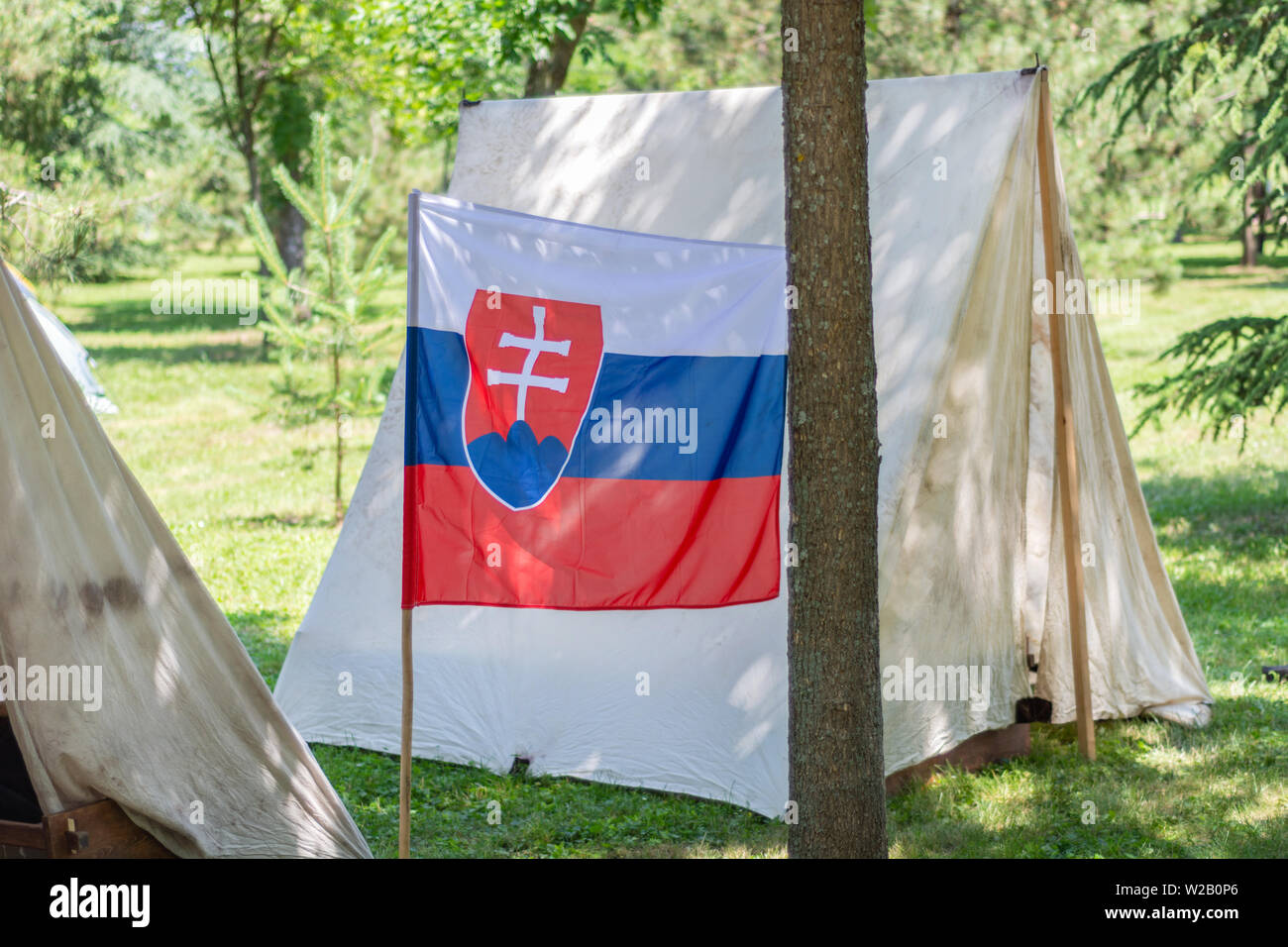 Drapeau de la Slovaquie et camp tente dans une forêt dans la nature sur une journée ensoleillée. Camping et rétro tente sous ombre d'une forêt de pins en Europe Banque D'Images