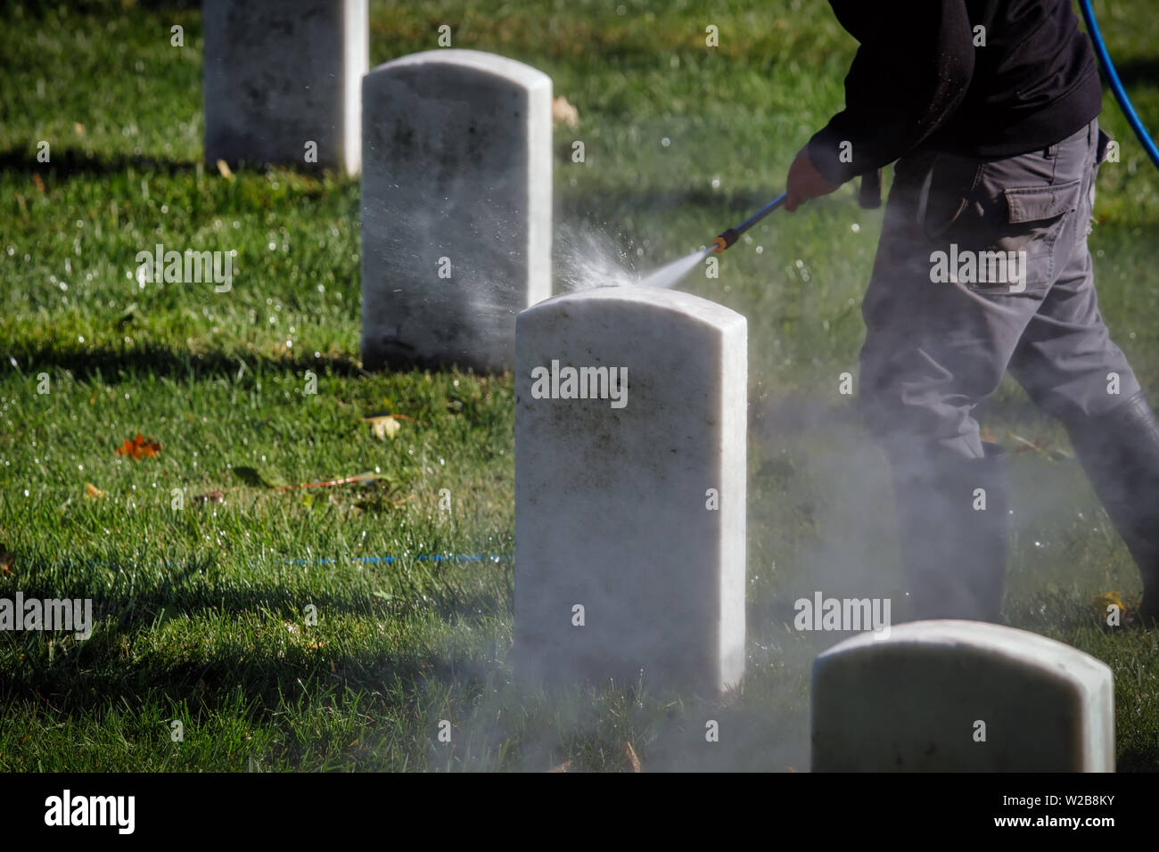 Un travailleur à un cimetière national de pierres tombales nettoyage avec un nettoyeur haute pression. Banque D'Images