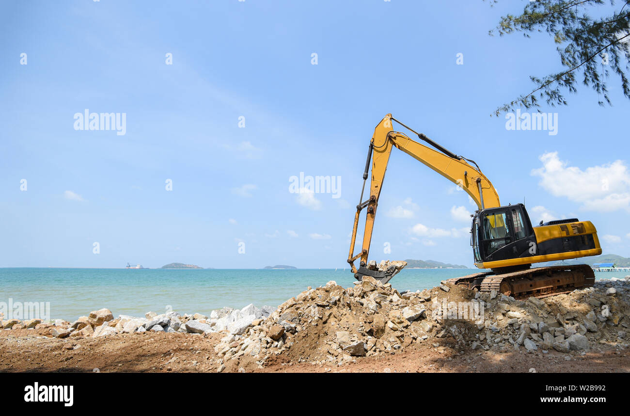 Pierre pelle digger working on construction site / chargeuse-pelleteuse sur la plage mer océan et fond de ciel bleu Banque D'Images