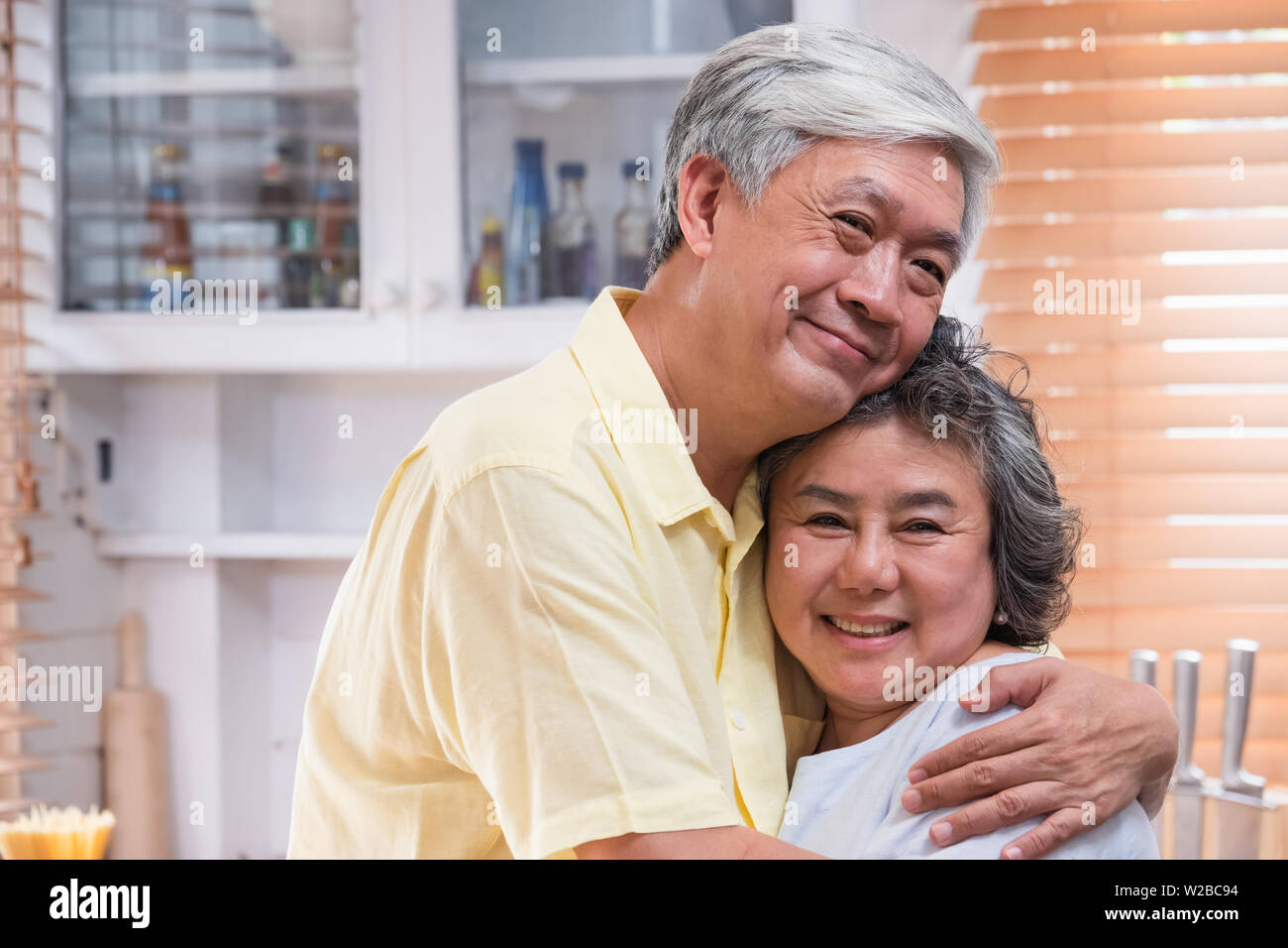Asian senior couple embrasser togerther et looking at camera and smiling in kitchen à la maison.Happy aging de home concept Banque D'Images