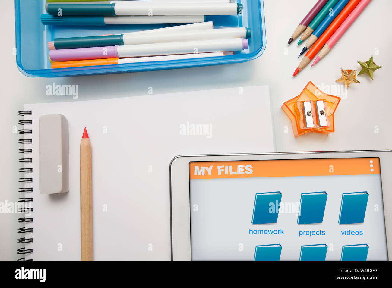 Fournitures scolaires des élèves avec une tablette graphique montrant les dossiers des étudiants en ligne, un blanc sketchpad avec crayons de couleur et des marqueurs. Banque D'Images