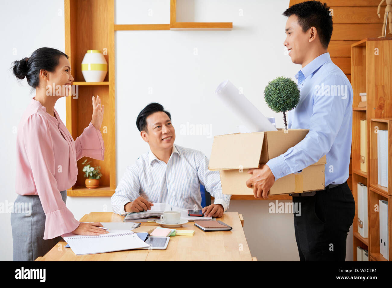 Heureux les jeunes gens d'affaires asiatiques leurs souhaits nouveau jeune collègue avec un carton d'effets personnels à l'office de tourisme Banque D'Images