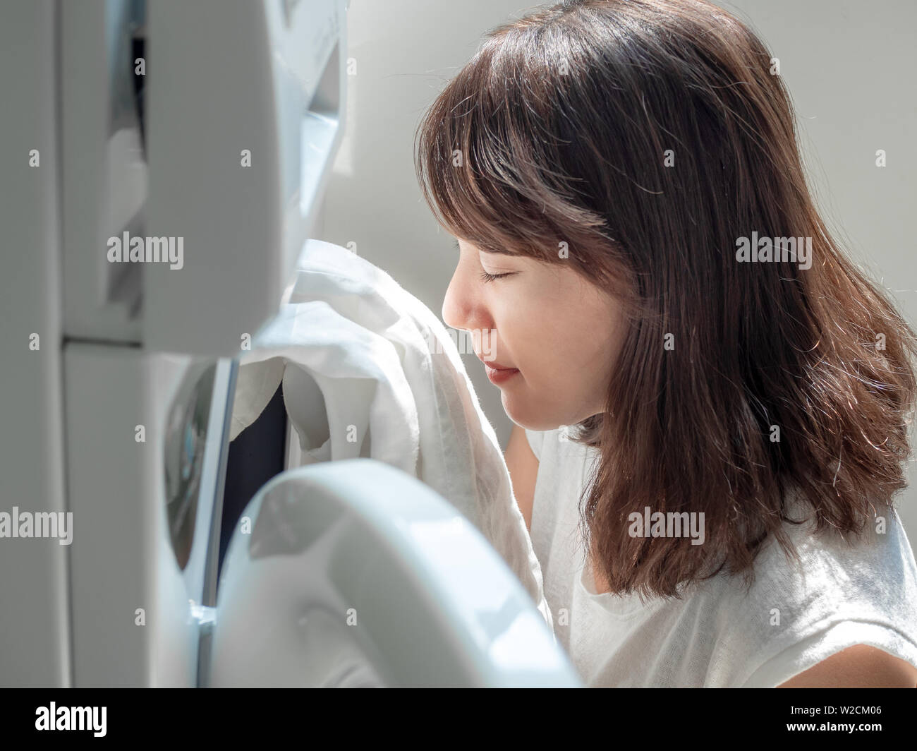 Close-up beautiful Asian woman smiling et sentir propre chemise en lin blanc après lavage d'un lave-linge. Banque D'Images