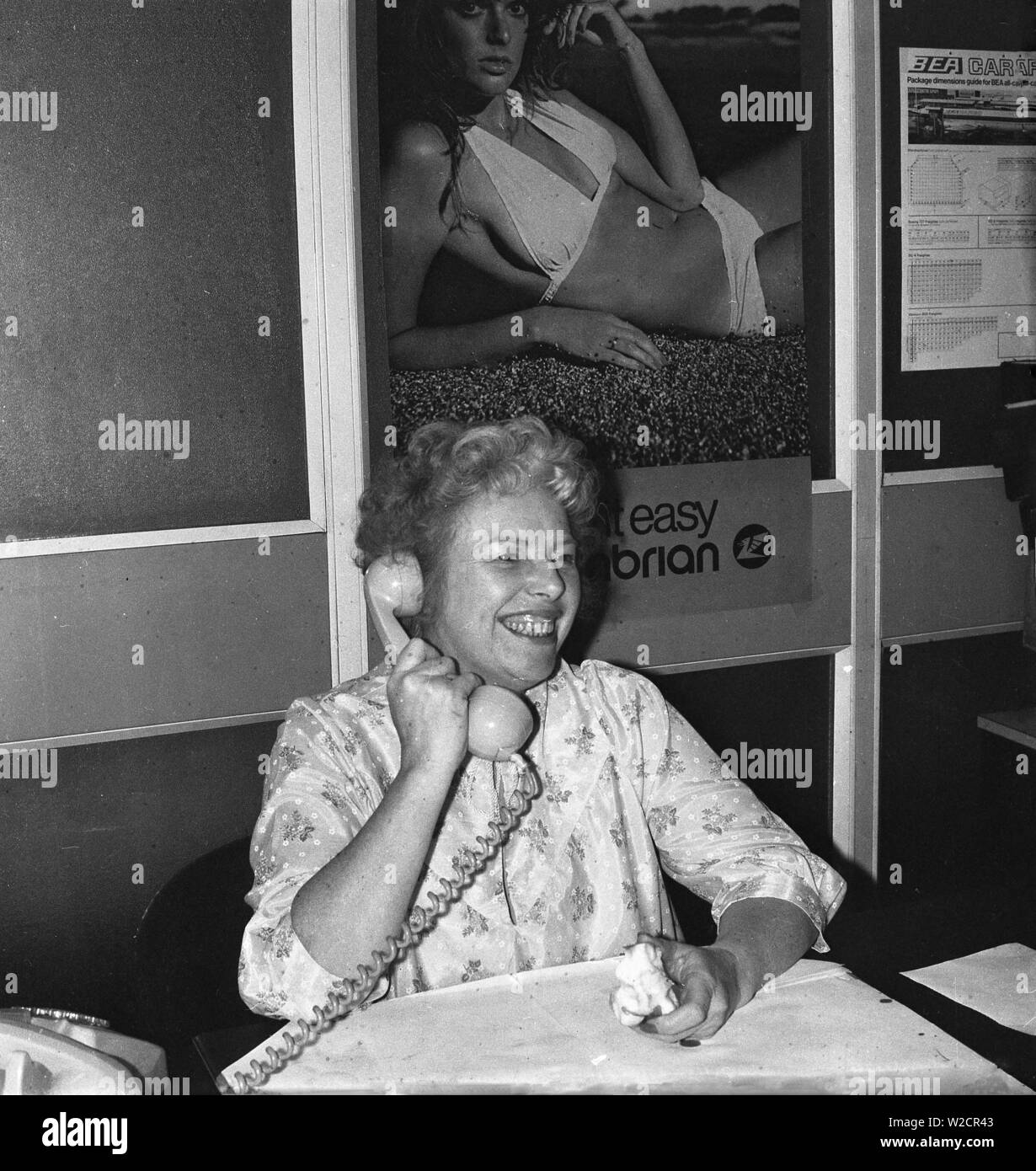 1974, historique, une dame à un bureau travaillant dans le bureau d'un agent de voyage, parlant au téléphone, Angleterre, Royaume-Uni. Banque D'Images