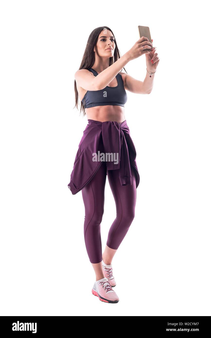 Fier jeune femme fitness confiant en tenant avec selfies téléphone mobile après exercices de gymnastique. Corps plein isolé sur fond blanc. Banque D'Images