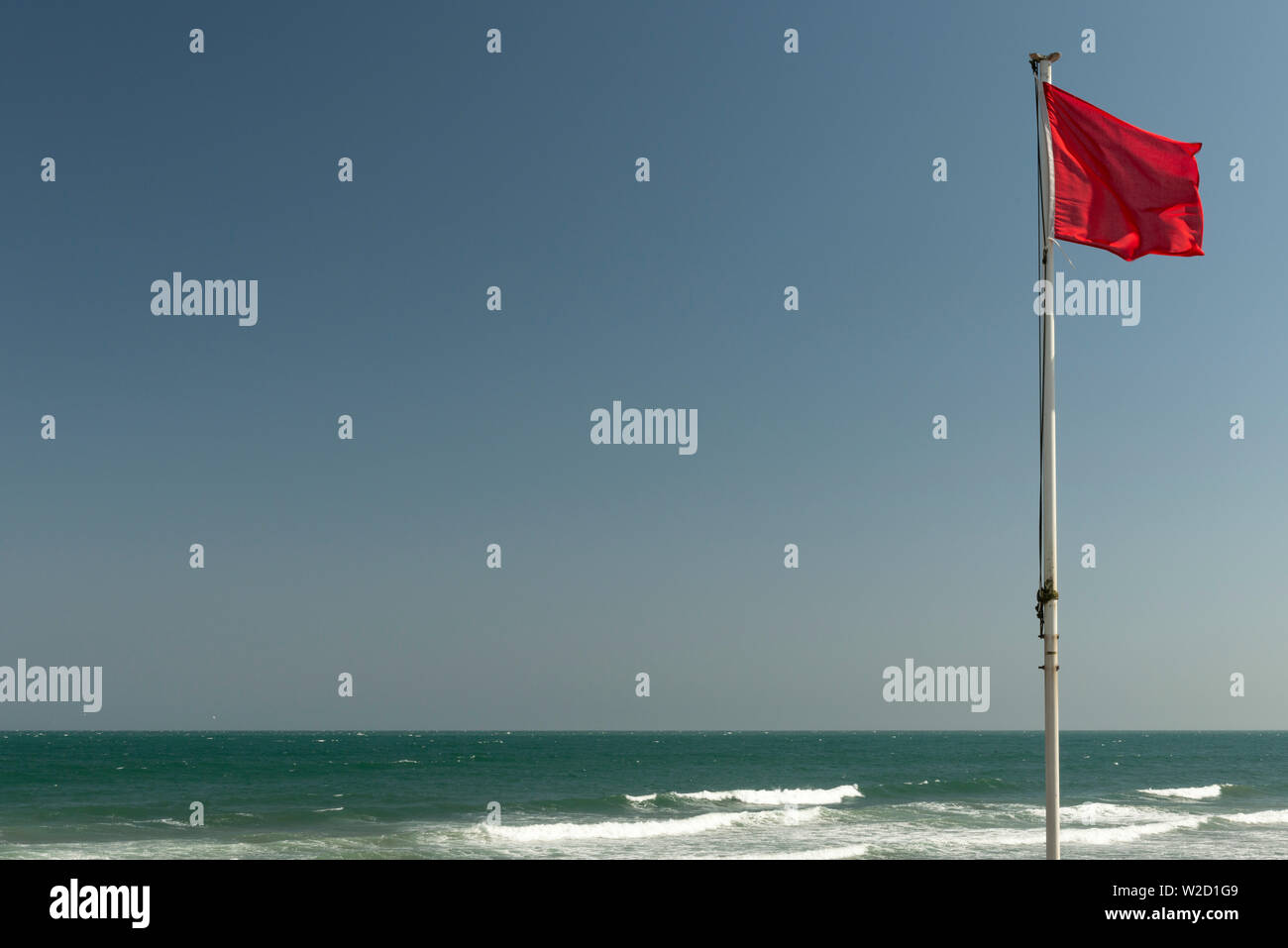 Drapeau rouge contre le ciel bleu et la mer ouverte à Youghal Strand, Comté de Cork, Irlande Banque D'Images