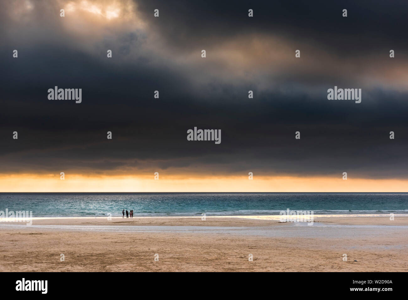 Un groupe de personnes flâner sur la plage dans un beau coucher du soleil à golden dans Fistral Newquay en Cornouailles. Banque D'Images