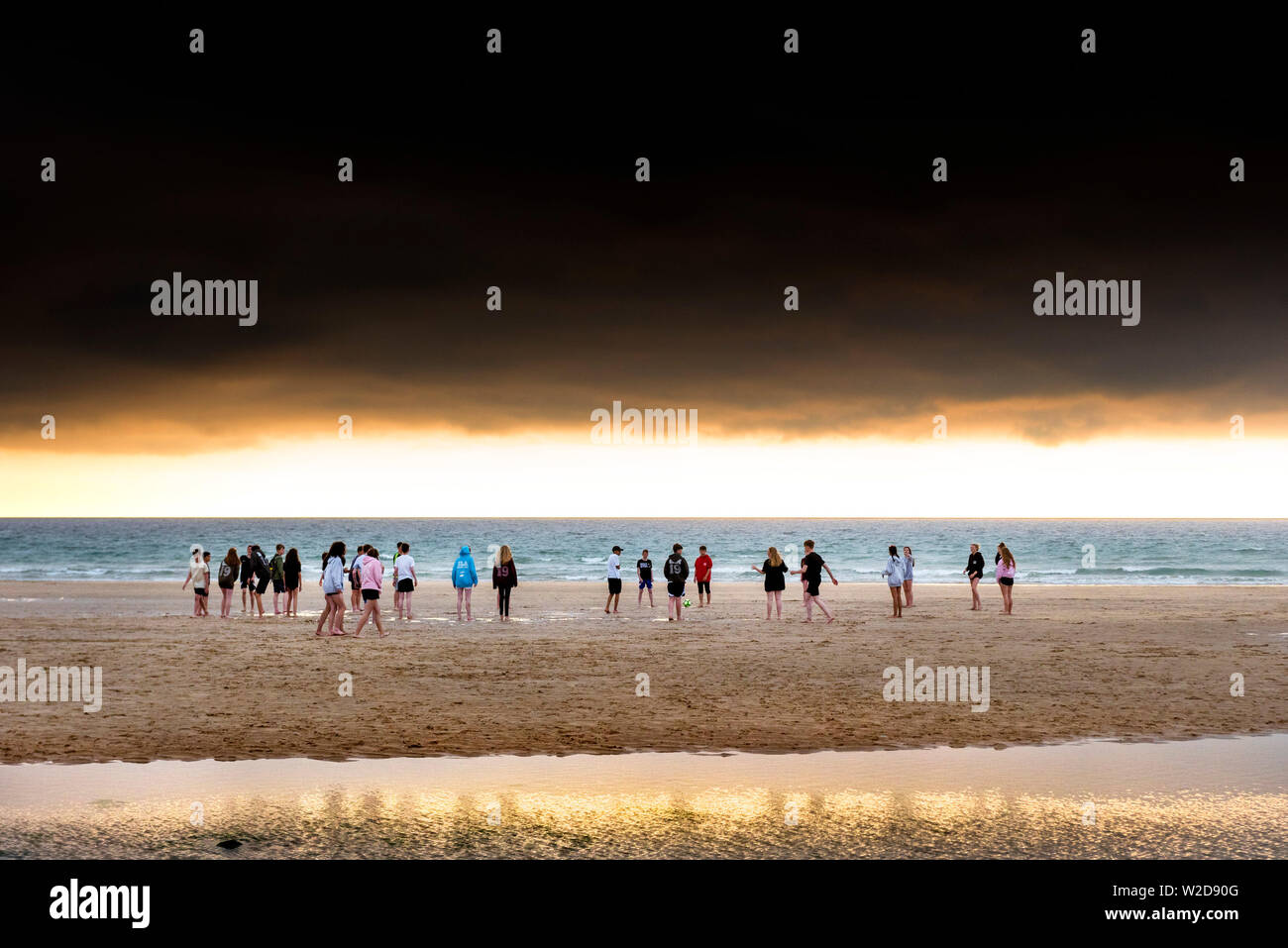 Un groupe d'adolescents flâner sur la magnifique plage de Fistral au coucher du soleil d'or à Newquay en Cornouailles. Banque D'Images