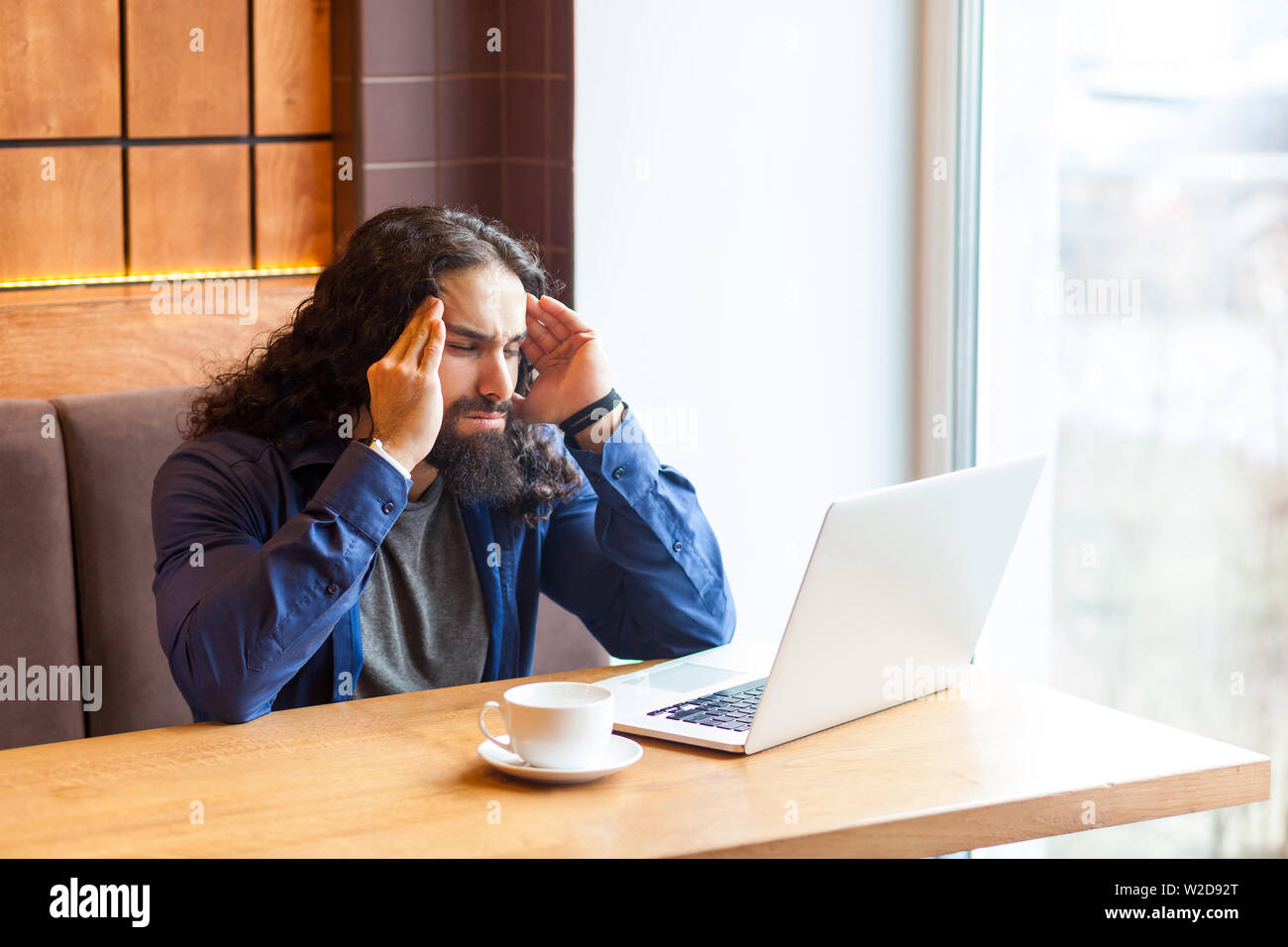 Portrait of handsome young adult man freelancer dans style casual assis dans un café avec un ordinateur portable, essayant de se concentrer et à se souvenir de certains d'informer Banque D'Images