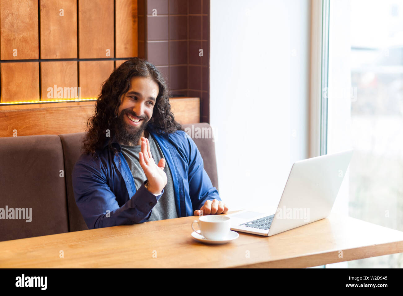 Bonjour ! Portrait de heureux beau jeune homme adulte freelancer dans style casual assis dans un café et parler avec son ami dans le coffre, montrant au revoir ges Banque D'Images