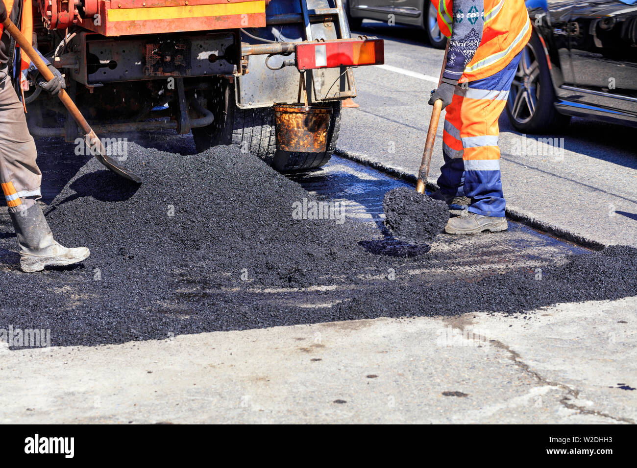 Le groupe de travail des travailleurs de la route met à jour la partie de la route avec de l'asphalte chaud avec des pelles et la répartit uniformément sur la surface. Banque D'Images