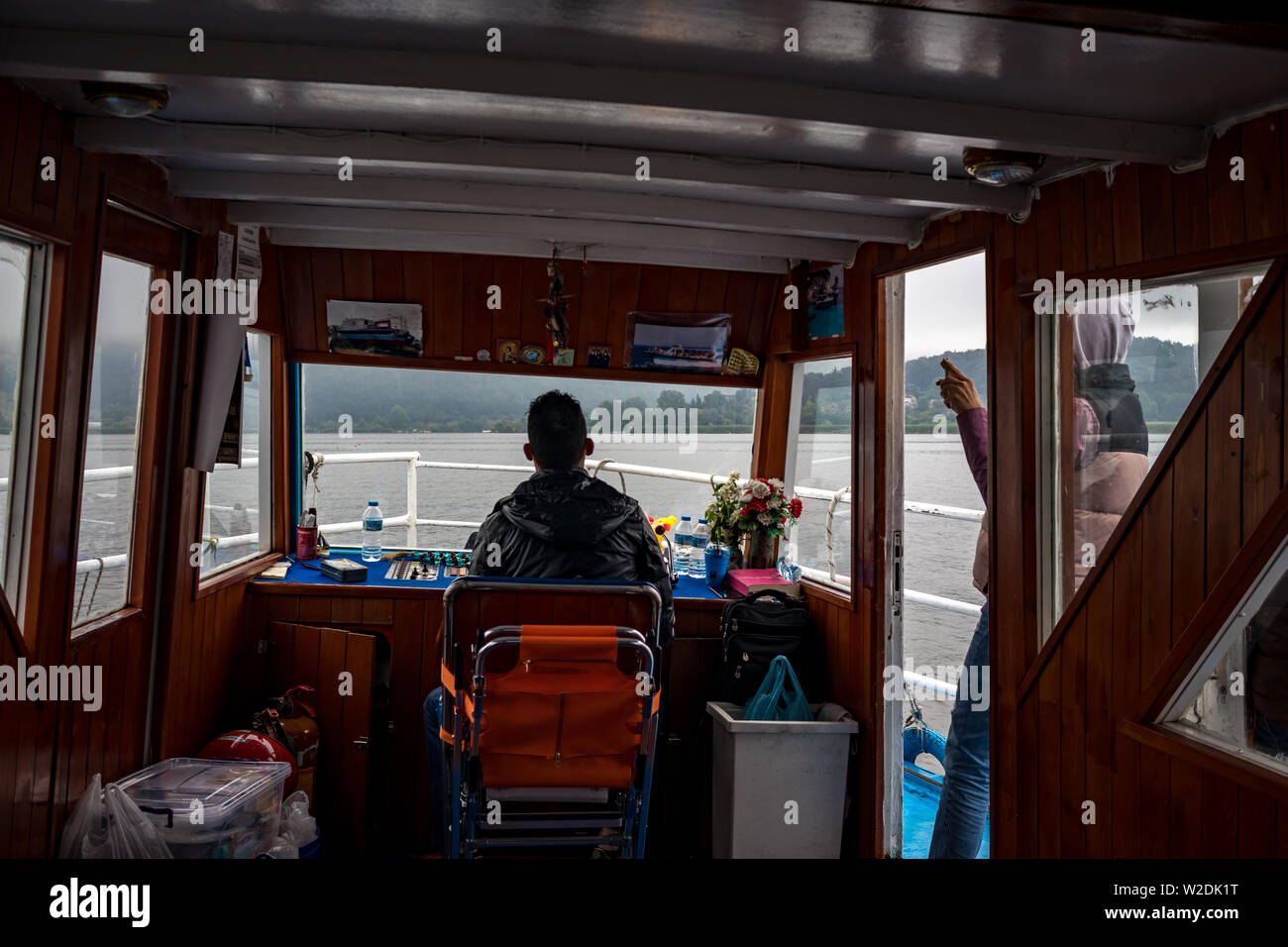 IOANNINA, GRÈCE - le 6 juin 2019 - le capitaine masculin petites règles blanc et rouge vieux ferry croisière touristique sur le lac Pamvotis près de la belle petite ville grecque. Vue arrière à l'intérieur de la cabine. Matin brumeux Banque D'Images