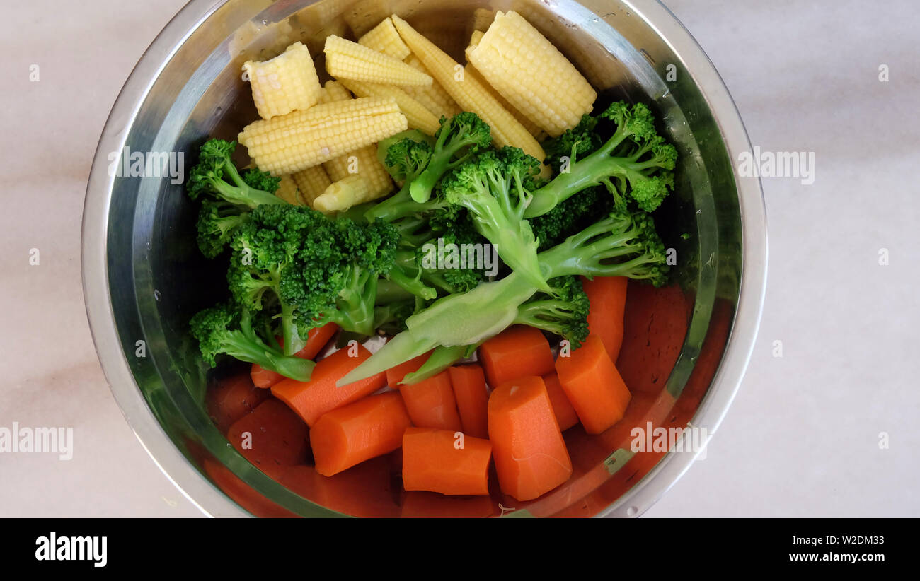 Mélange de légumes carottes, brocoli et mini-maïs disposés selon les couleurs, dans un bol en métal. Banque D'Images