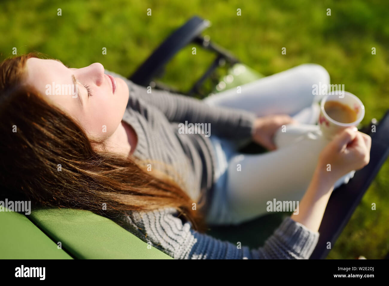 Woman relaxing with closed eyes et tasse de café dans une chaise longue sur une journée ensoleillée à l'extérieur, la rêverie. Banque D'Images