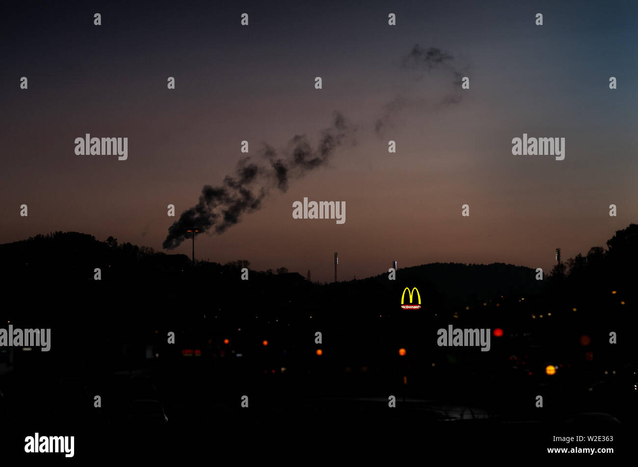 Une épaisse fumée noire sur les toits de la ville de Duck avec un McDonalds signer brillants dans l'arrière-plan. Banque D'Images
