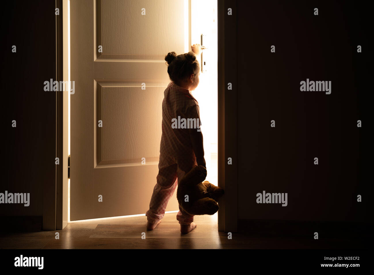Petite fille ouvre la porte à la lumière dans l'obscurité. Banque D'Images