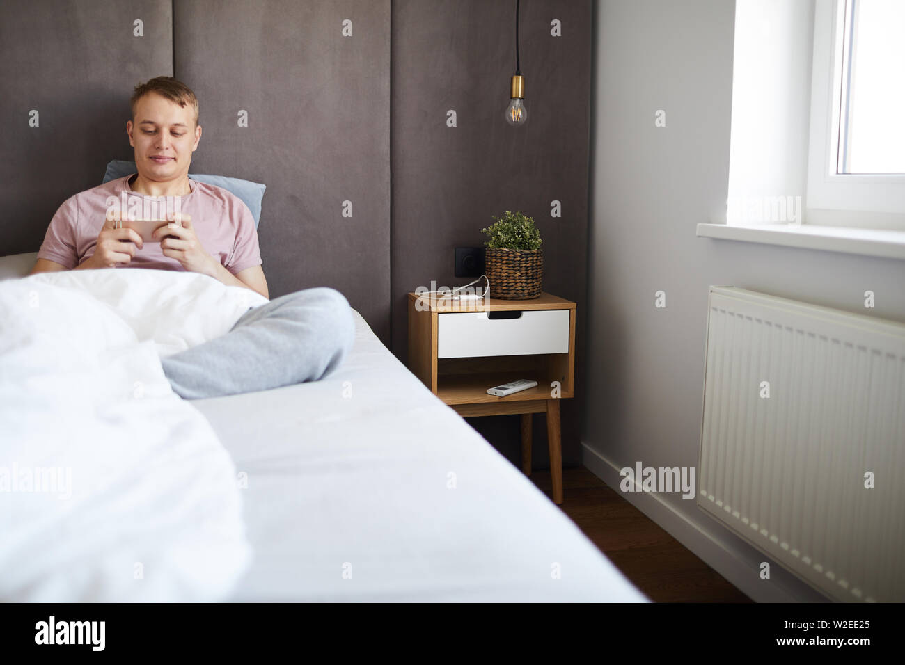 Heureux guy détendue assis au lit sous couverture et regarder la vidéo en curieux à loisir smartphone Banque D'Images