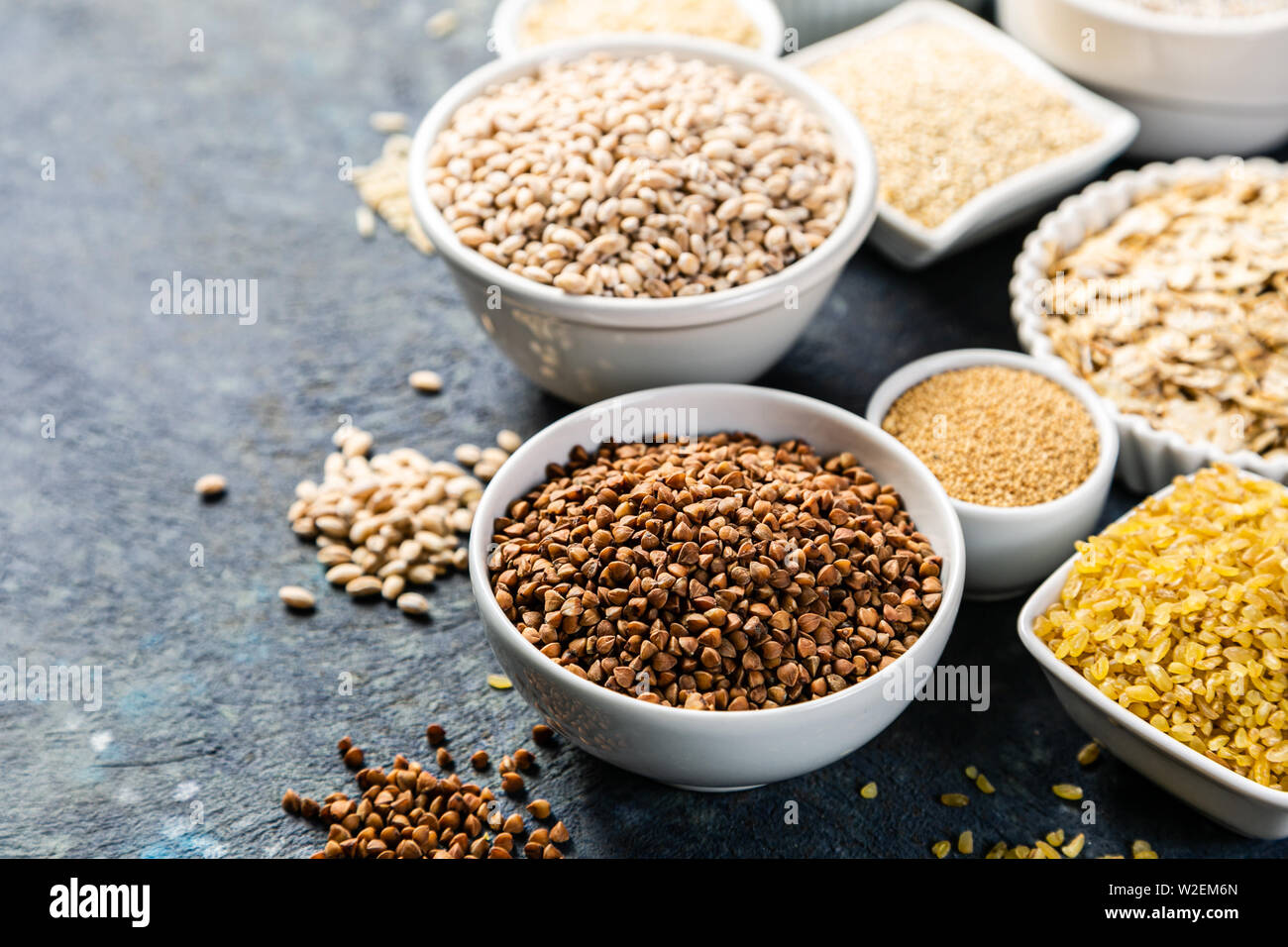 Sélection de grains entiers dans des bols blancs : riz, avoine, sarrasin, boulgur, porridge, orge, quinoa, amarante Banque D'Images