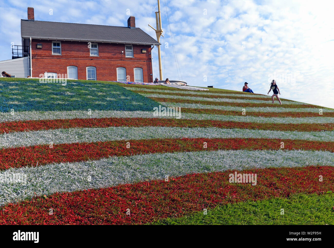 Un drapeau américain géant peint dans l'herbe sur une colline à Fairport Harbor, Ohio, USA donne un peu de gens un point d'observation pour voir les feux d'artifice 2019. La colline a été peint en l'honneur de l'US le 4 juillet au cours de laquelle Fairport Harbor sur le lac Érié accueille un événement de plusieurs jours qui a culminé dans la soirée du 7 juillet avec un feu d'artifice. Banque D'Images