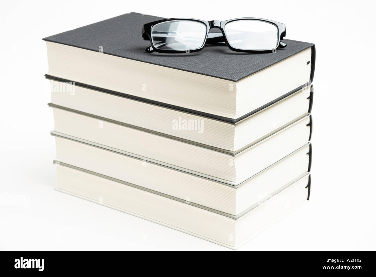 Une pile de série de cinq livres reliés en tissu monochrome avec des lunettes de lecture sur un arrière-plan uni, blanc. Banque D'Images