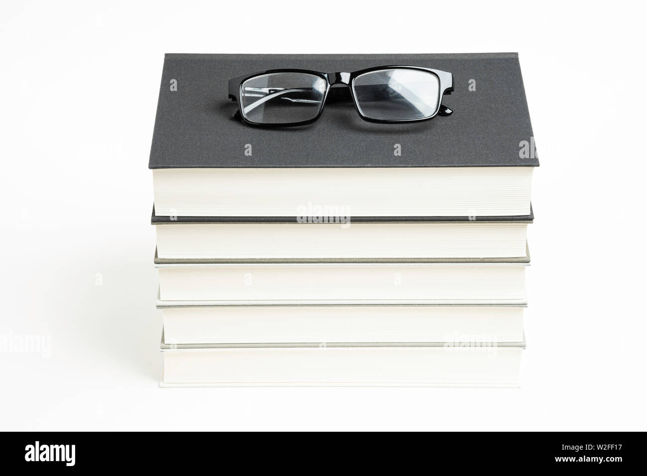 Une pile de série de cinq livres reliés en tissu monochrome avec des lunettes de lecture sur un arrière-plan uni, blanc. Banque D'Images