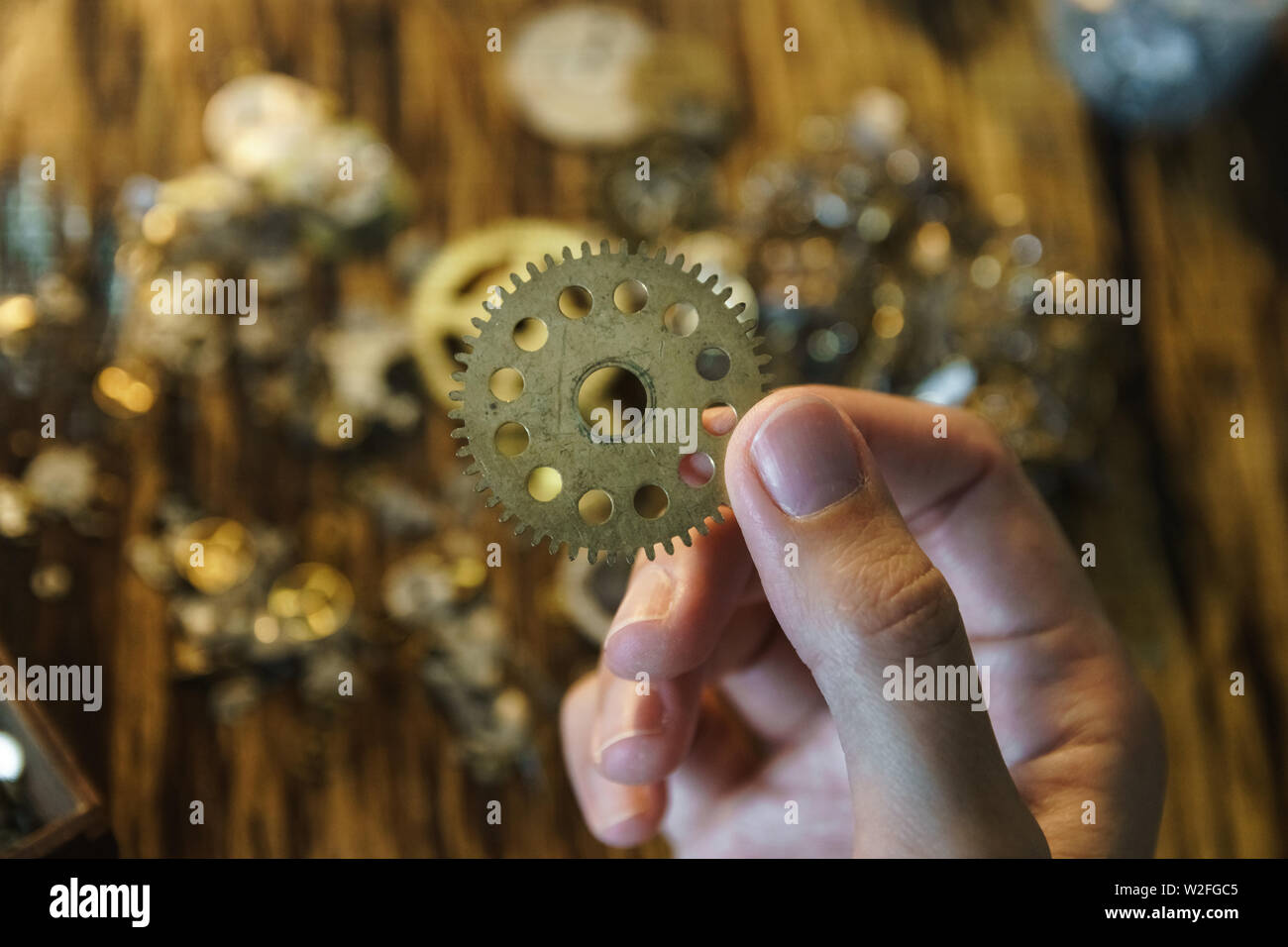 Watch reparateur détient le grand pignon. Grande roue de métal sur l'espace flou. Roue dentée sur l'arrière-plan flou de travail. Main de femme en pignon. Banque D'Images