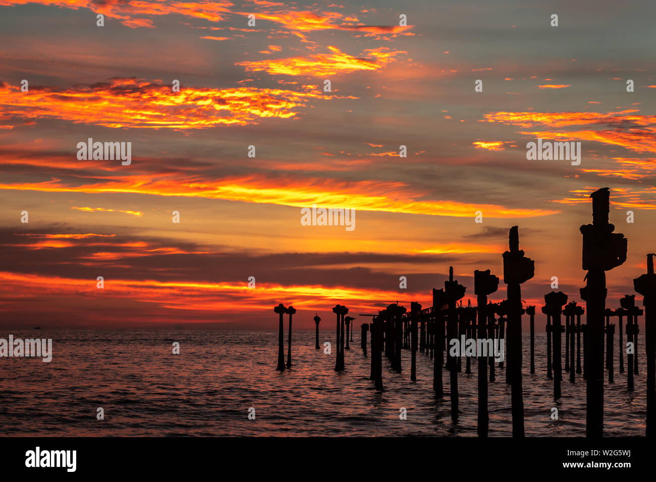 Nuages orange sur l'horizon de mer avec des poteaux de fer vers le soleil Banque D'Images