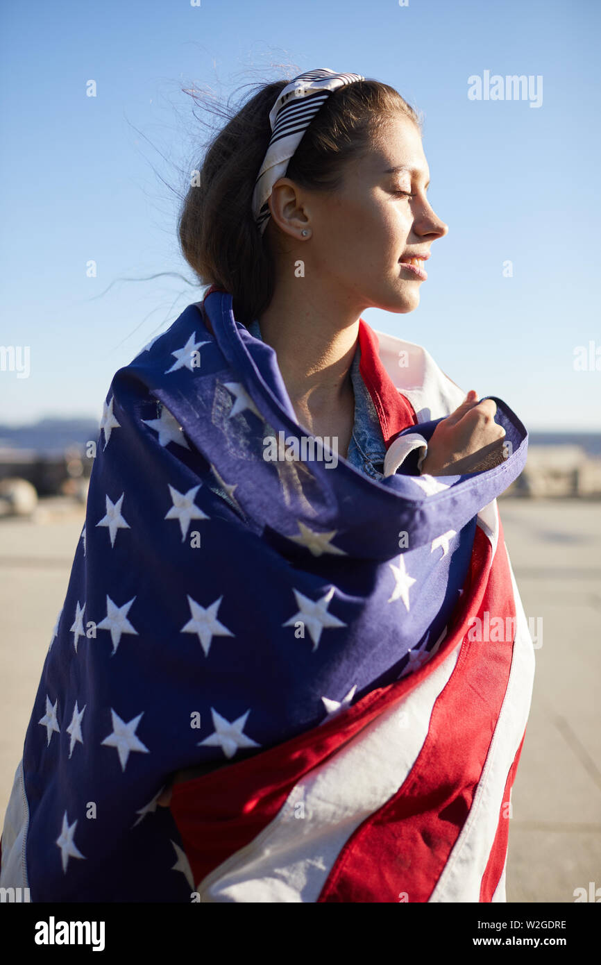 Smiling attractive young woman avec foulard dénudé couverts avec le drapeau  américain dans le vent debout à l'extérieur et en gardant les yeux fermés  tout en appréciant lei Photo Stock - Alamy
