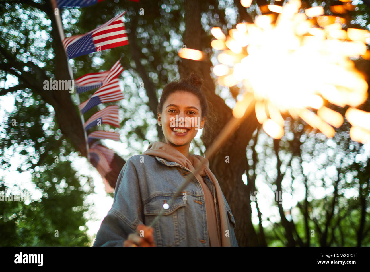 Portrait de jeune femme en extase in hoodie veste en jean et en marche du parc de la ville décorée de drapeaux américains, elle s'amuser le jour de l'indépendance de Banque D'Images