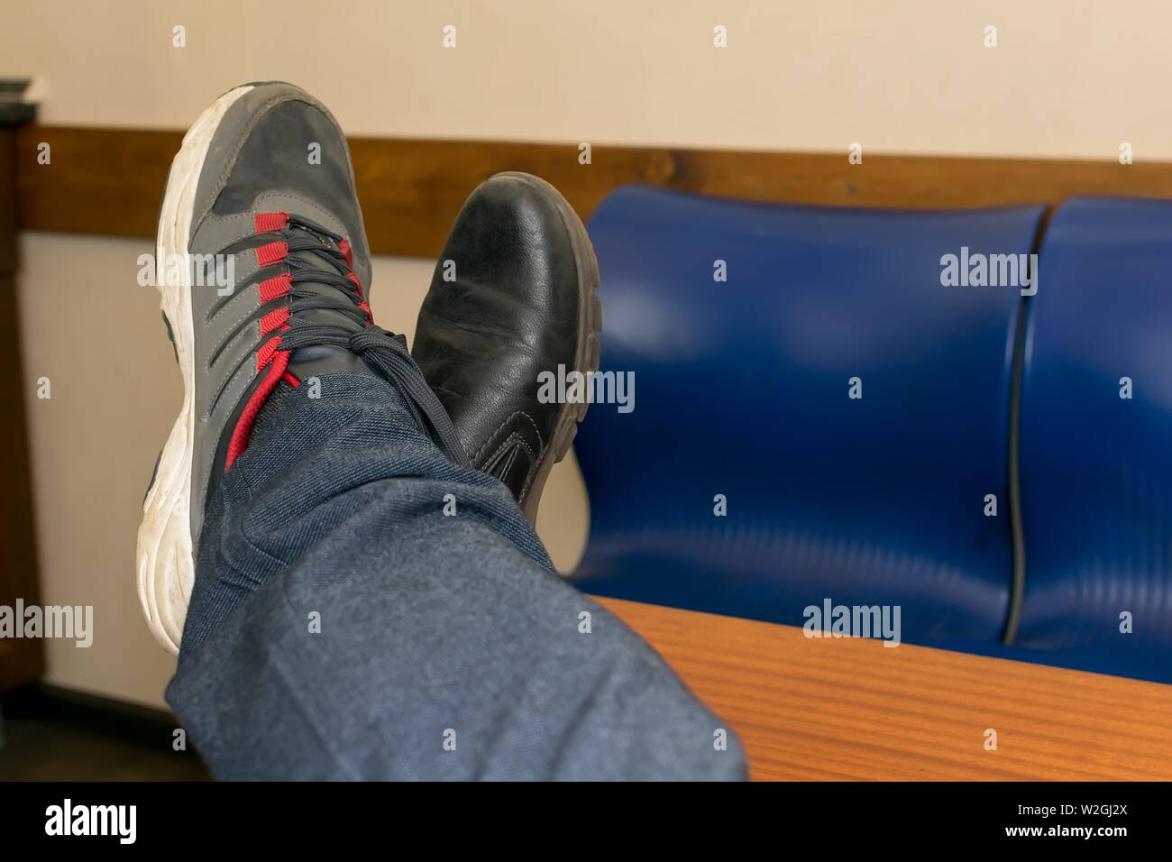 L'homme est assis avec ses pieds sur la table, qui sont chaussés par erreur dans des chaussures, chaussures et sneakers Banque D'Images