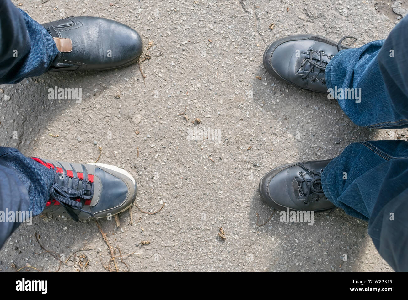 Les pieds des deux hommes debout sur une route asphaltée, un gars chaussés par erreur dans des chaussures, chaussures et sneakers Banque D'Images