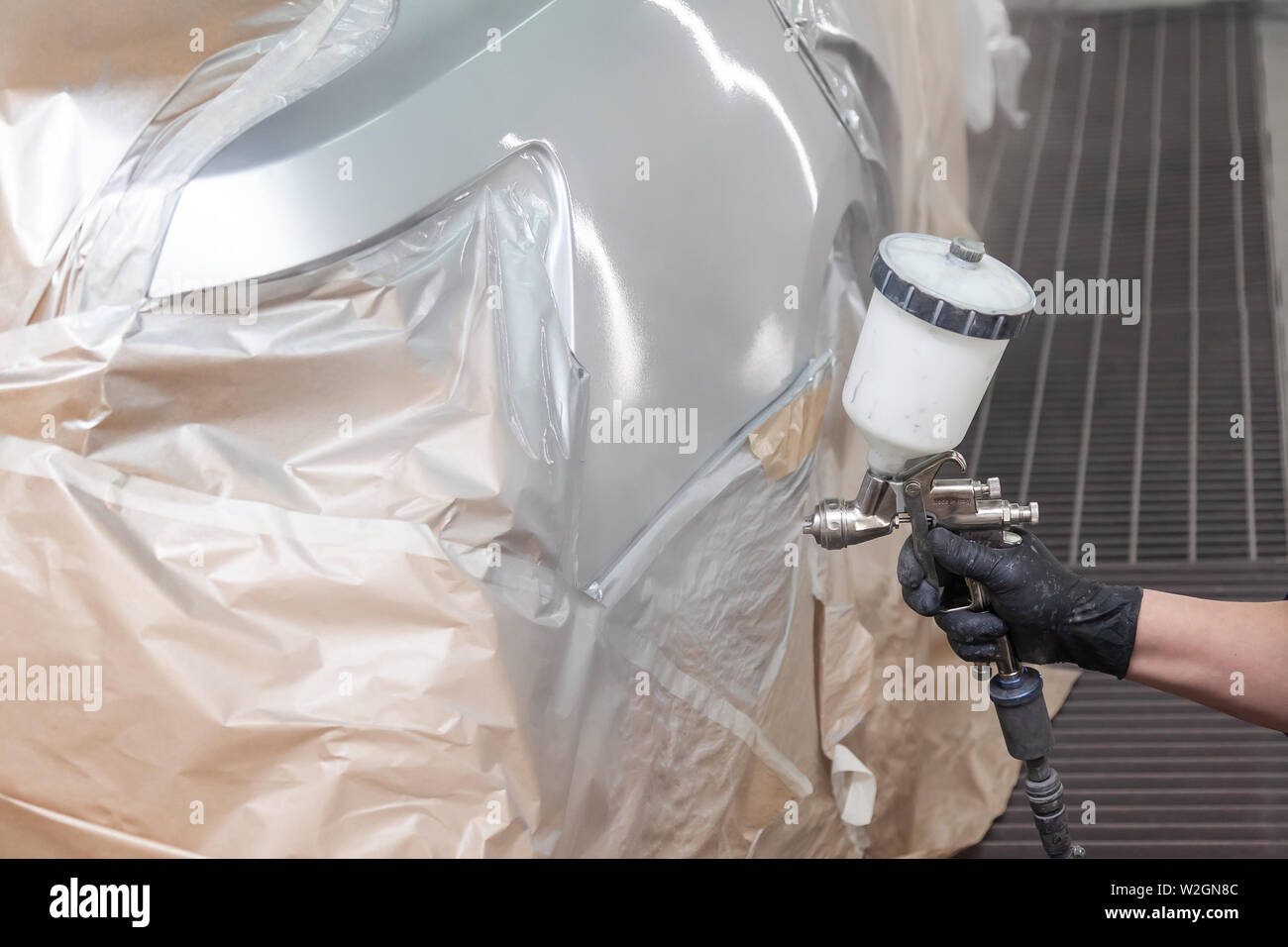 Un travailleur masculin peint avec un pistolet d'une partie de la carrosserie dans l'argent après avoir été endommagé lors d'un accident. À partir de l'aile arrière du véhicule pendant la rep Banque D'Images