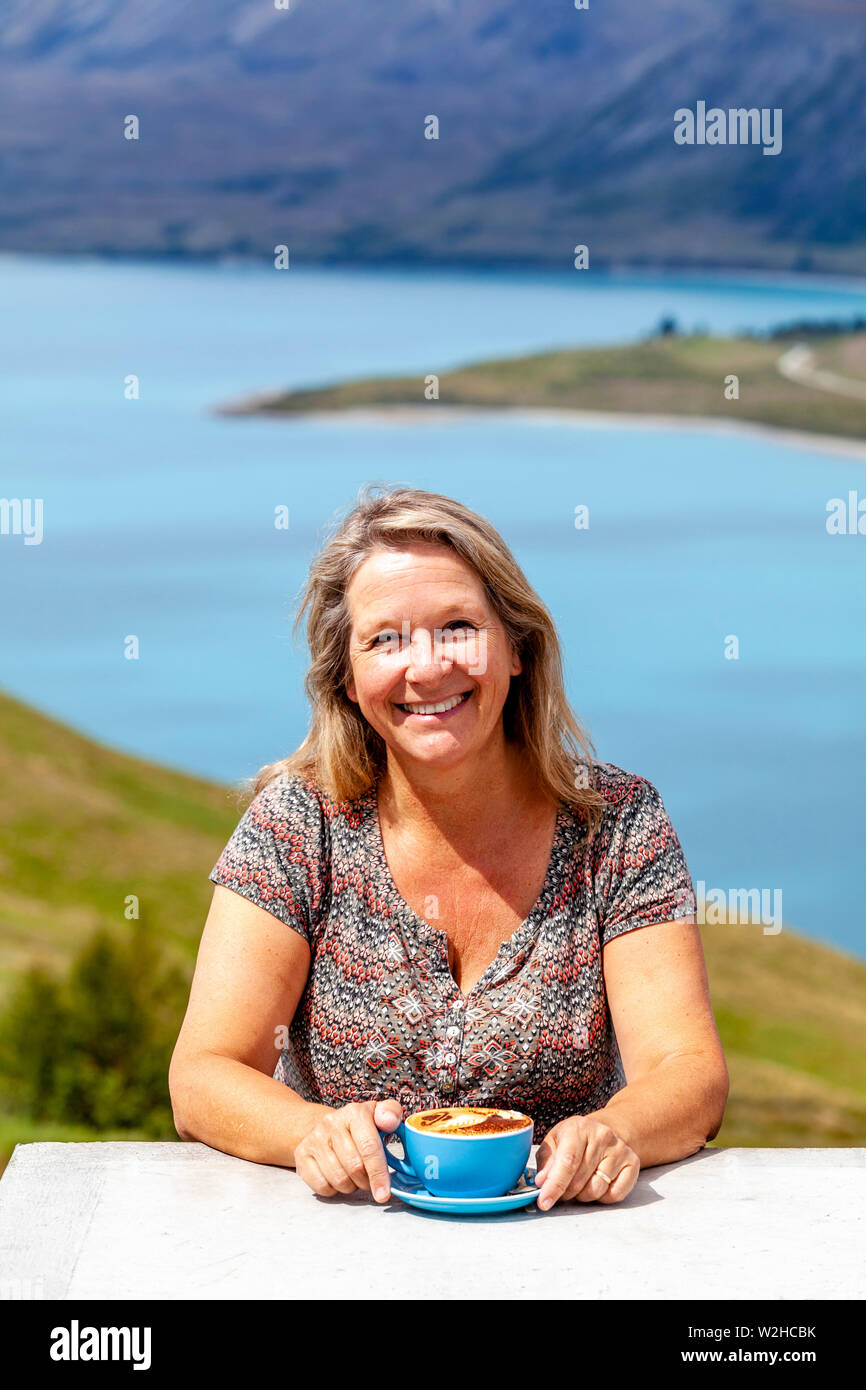 Une femme d'âge moyen assis avec une tasse de café avec vue sur le Lac Tekapo, Mt John Observatory de vue, District de Mackenzie, île du Sud, Nouvelle-Zélande Banque D'Images Une femme d'âge moyen assis avec une tasse de café avec vue sur le Lac Tekapo, Mt John Observatory de vue, District de Mackenzie, île du Sud, Nouvelle-Zélande Banque D'Images