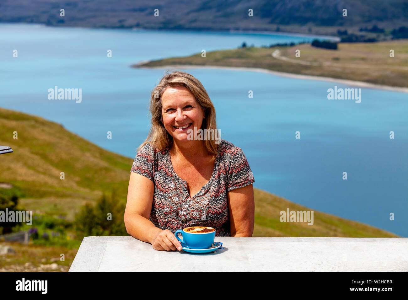 Une femme d'âge moyen assis avec une tasse de café avec vue sur le Lac Tekapo, Mt John Observatory de vue, District de Mackenzie, île du Sud, Nouvelle-Zélande Banque D'Images Une femme d'âge moyen assis avec une tasse de café avec vue sur le Lac Tekapo, Mt John Observatory de vue, District de Mackenzie, île du Sud, Nouvelle-Zélande Banque D'Images