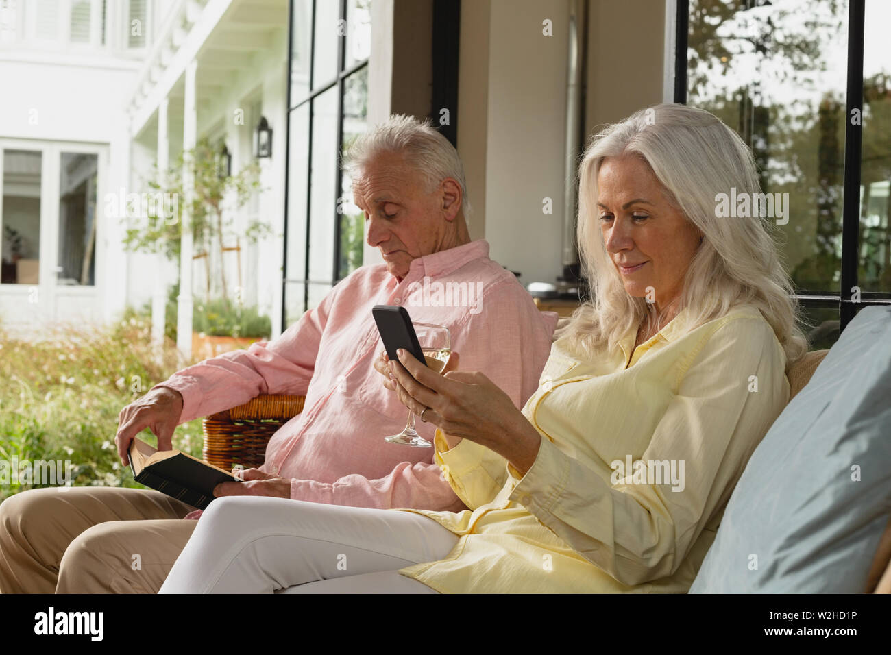 Senior couple using mobile phone et lire un livre dans la véranda Banque D'Images