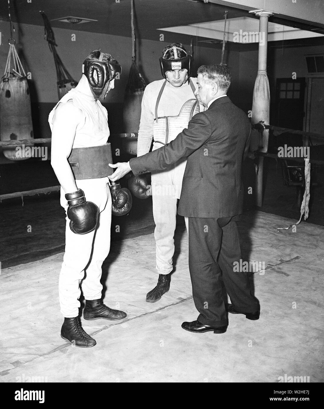 Homme en costume s'adressant à deux boxeurs sur le ring d'un club de boxe ca. 1936 Banque D'Images
